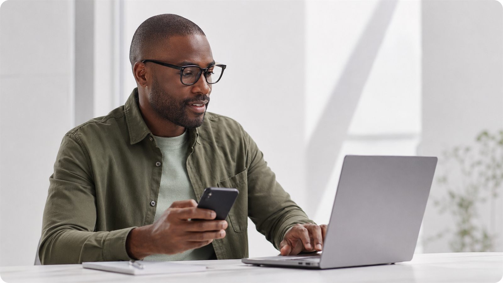 Business owner checking project status on his phone while working at a laptop
